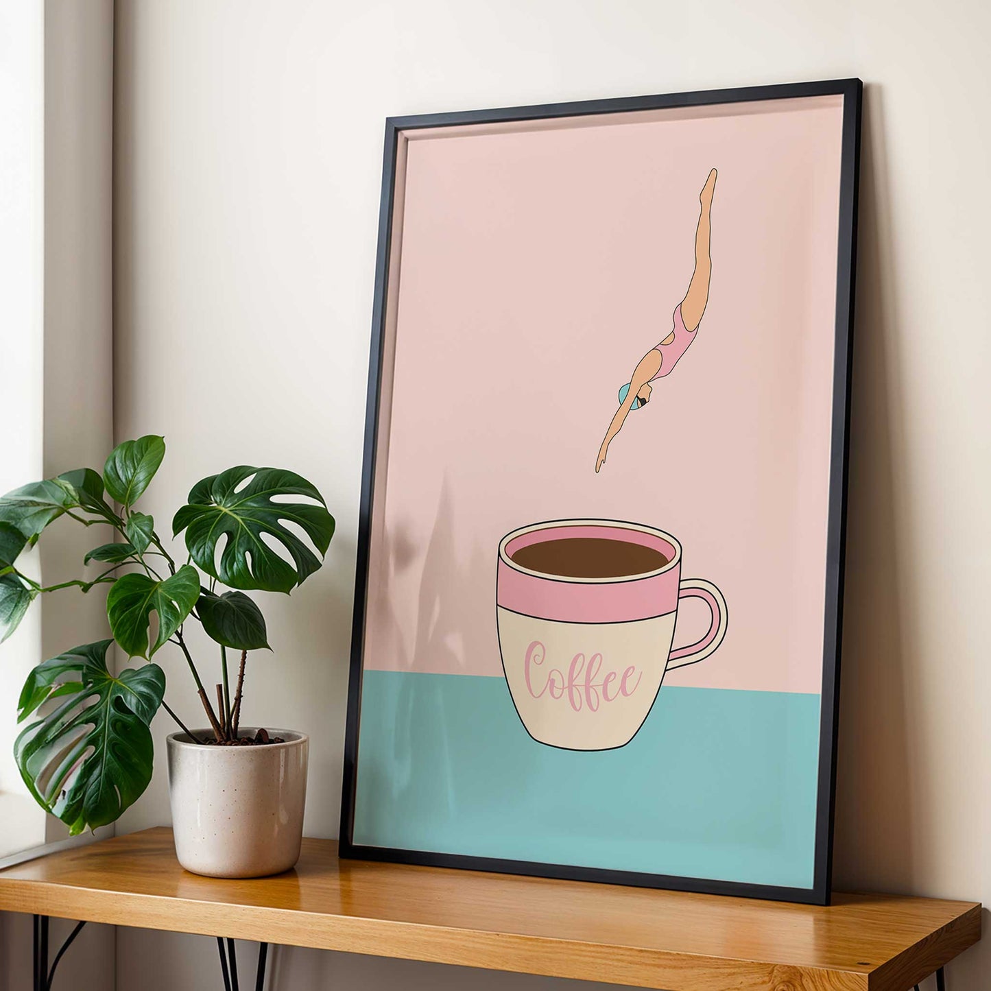 Framed artwork of a diver diving into a coffee cup with a plant on a table below.