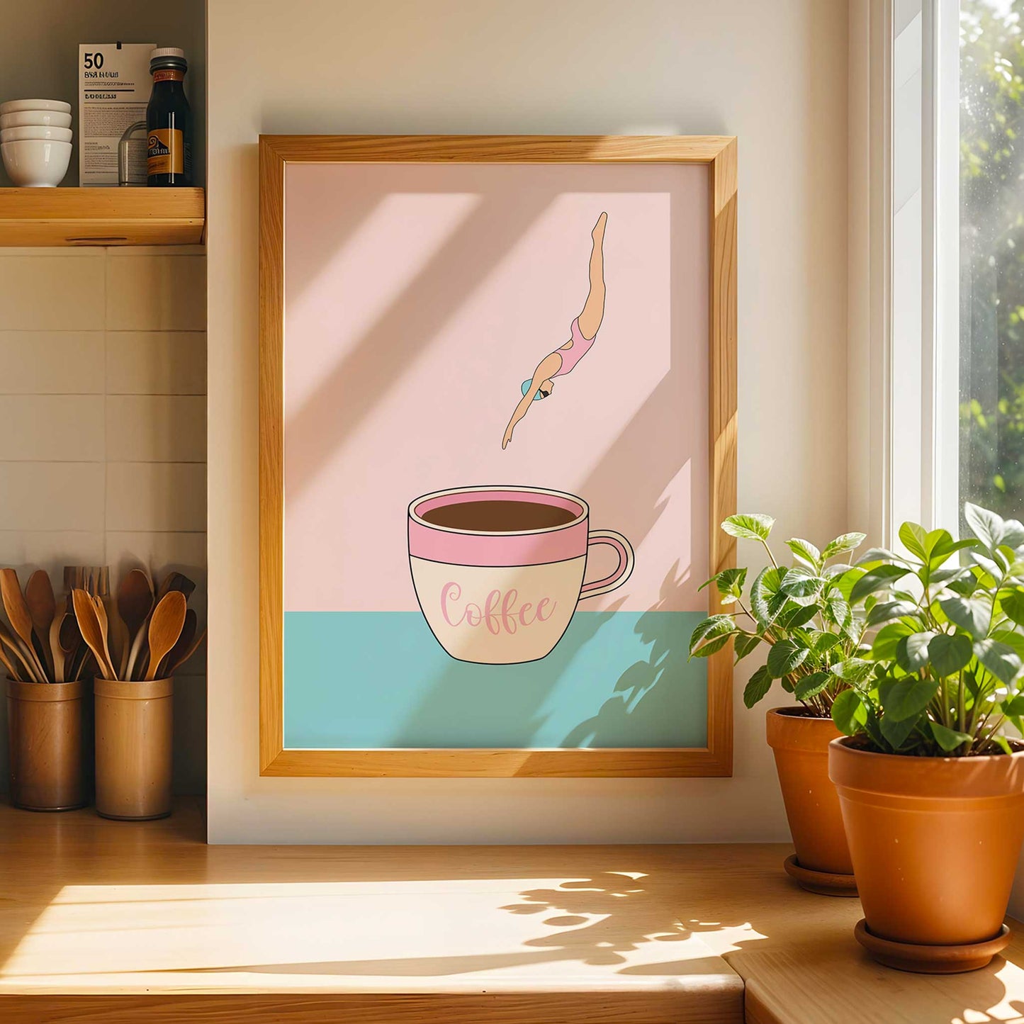 Framed artwork of a coffee cup with a person inside, placed on a kitchen counter with plants and utensils.