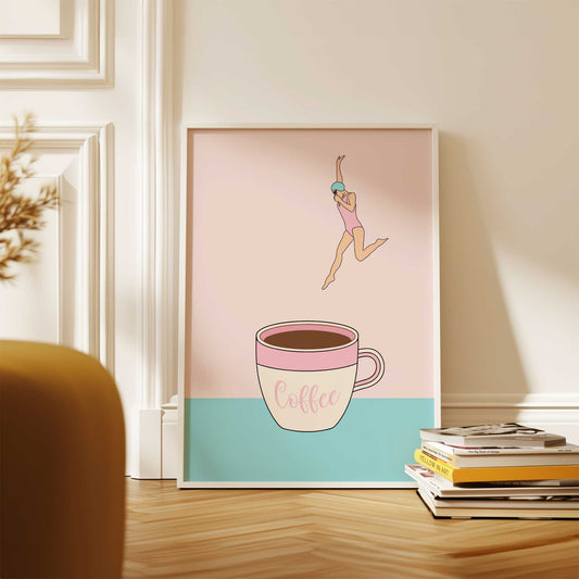 Framed artwork of a woman leaping over a coffee cup with 'coffee' text on a pink and blue background, placed on a wooden surface.